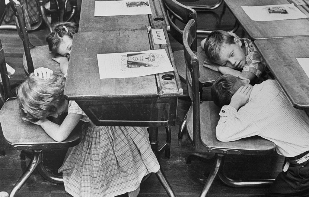 Black-and-white photo of children crouched under their school desks