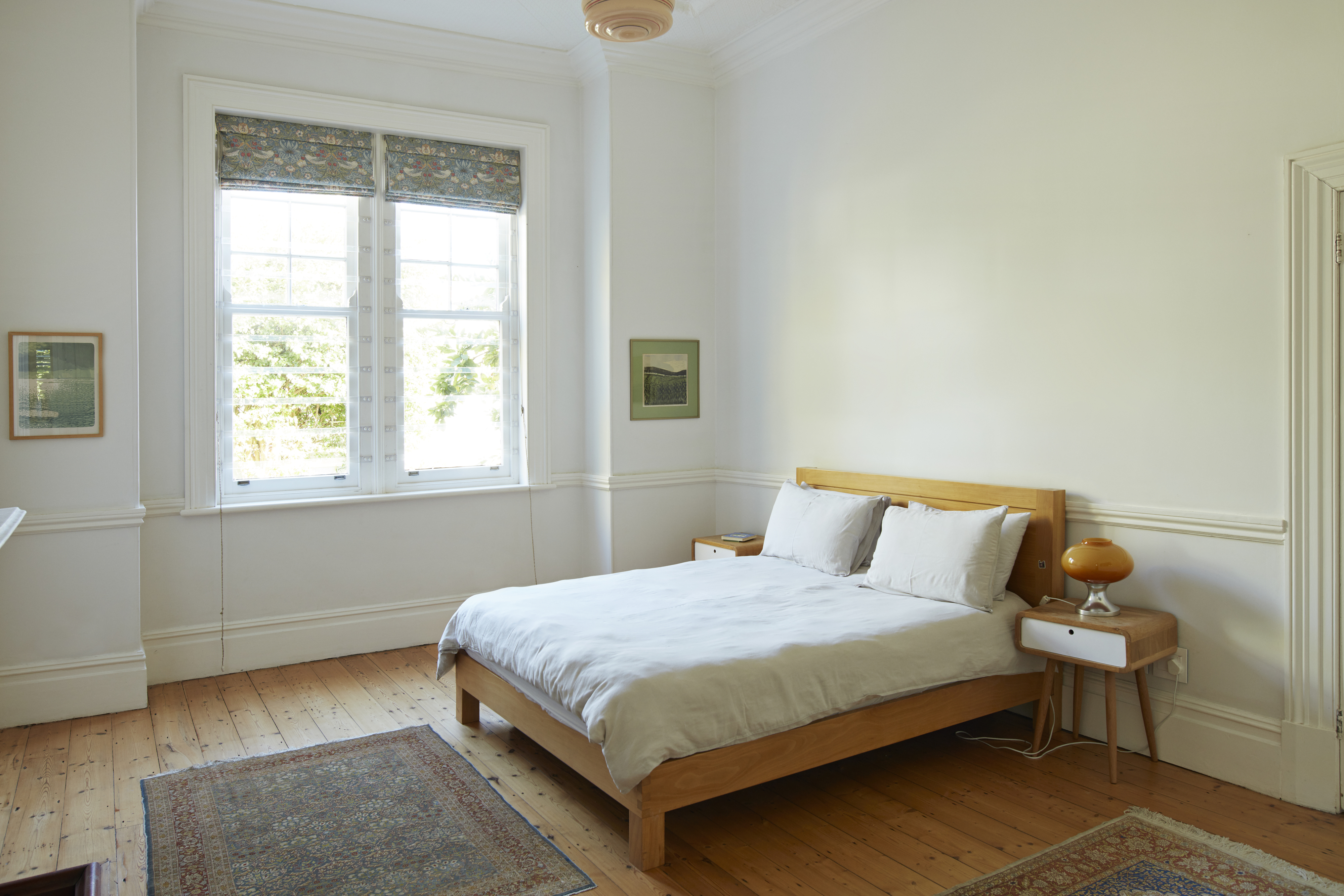 A bedroom with white walls, a platform wood bed, and white bedding