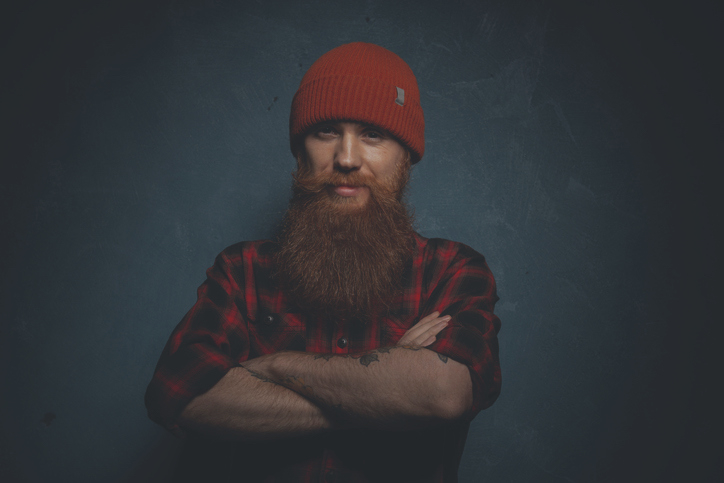 A person in a beanie, long beard, and flannel shirt with their arms folded