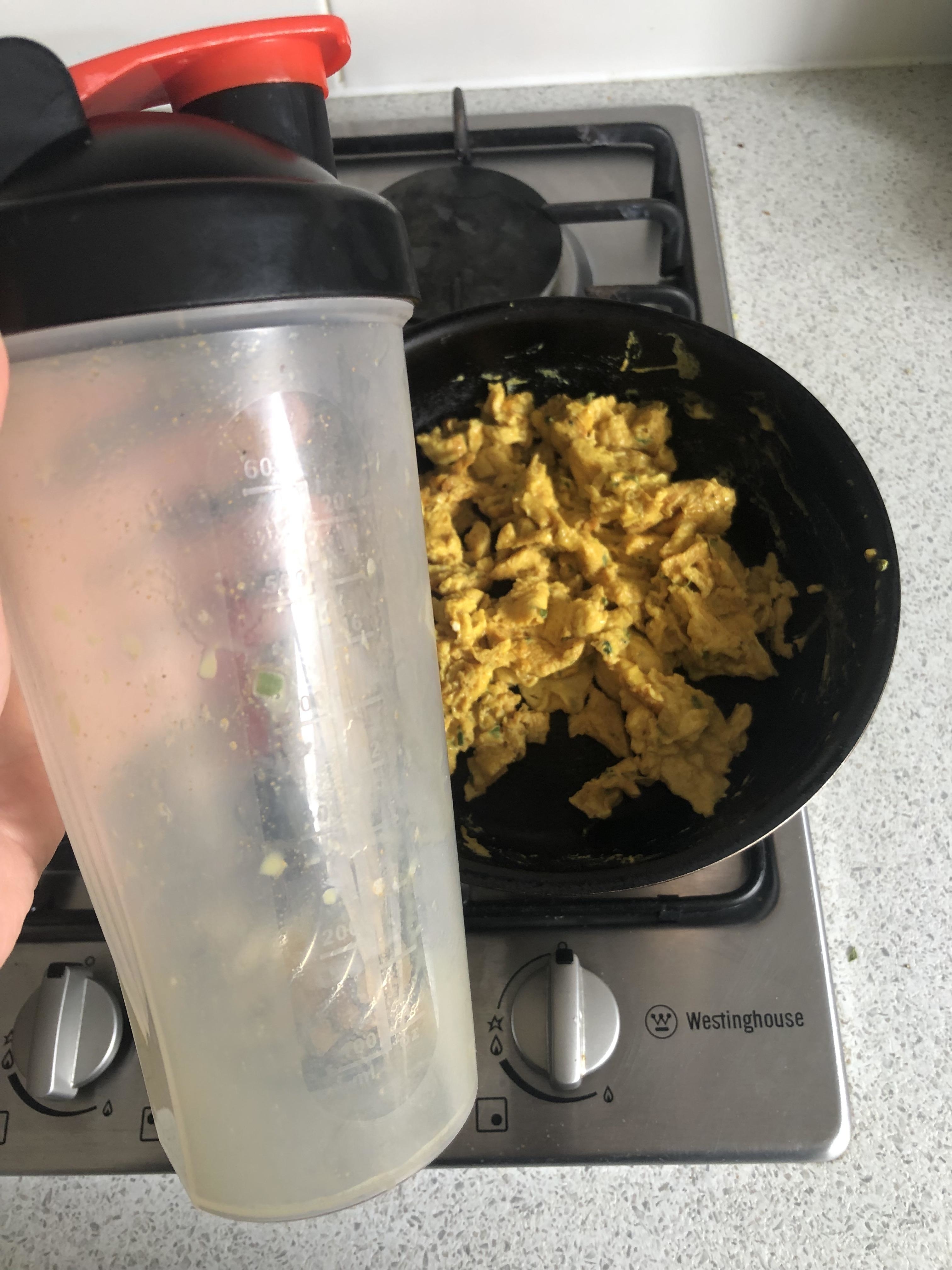Someone holding a protein shaker in front of eggs on the stove