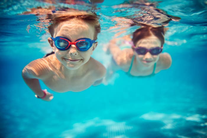 Two kids swimming underwater with goggles