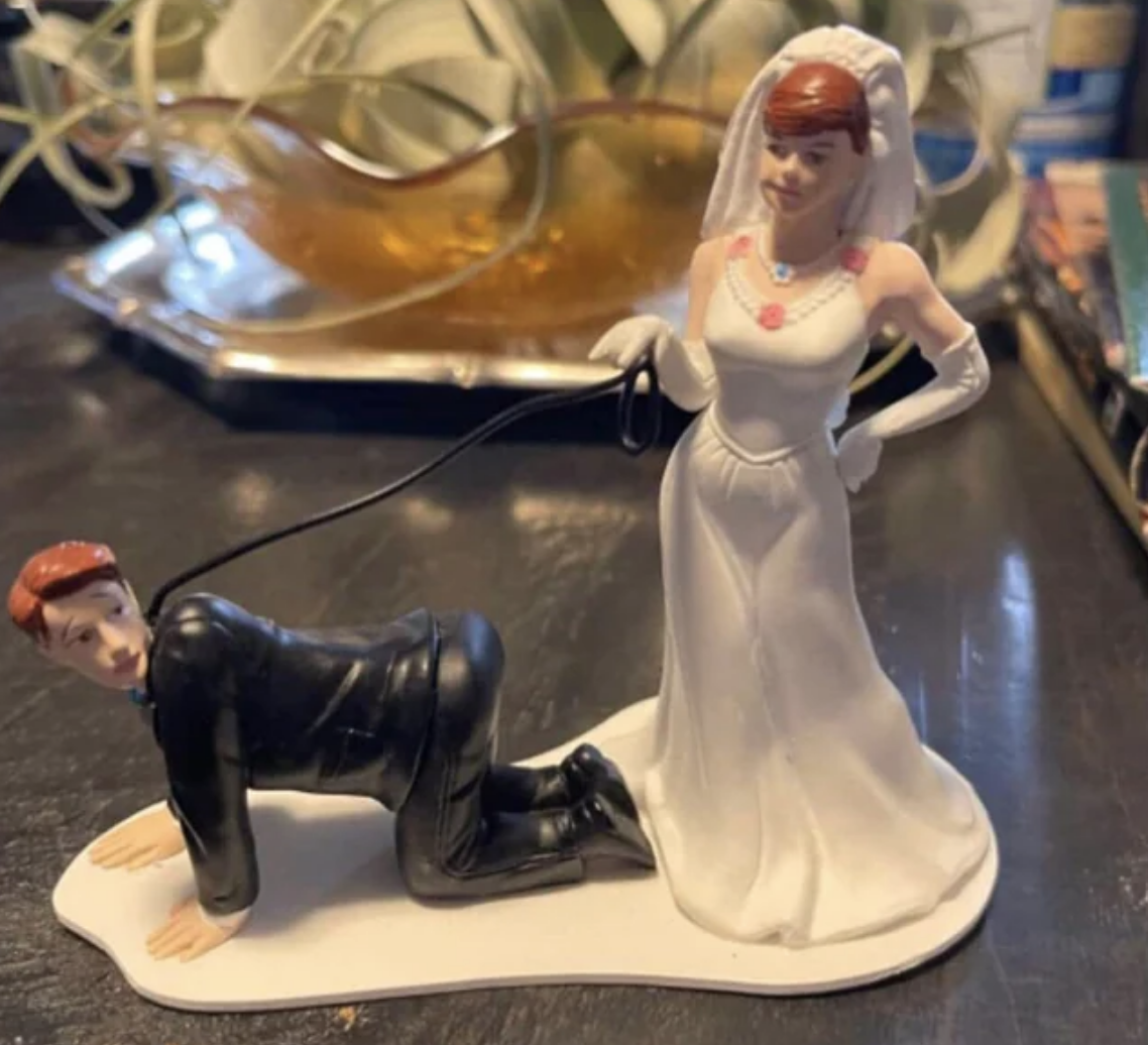 A cake topper where the bride has the groom on a leash