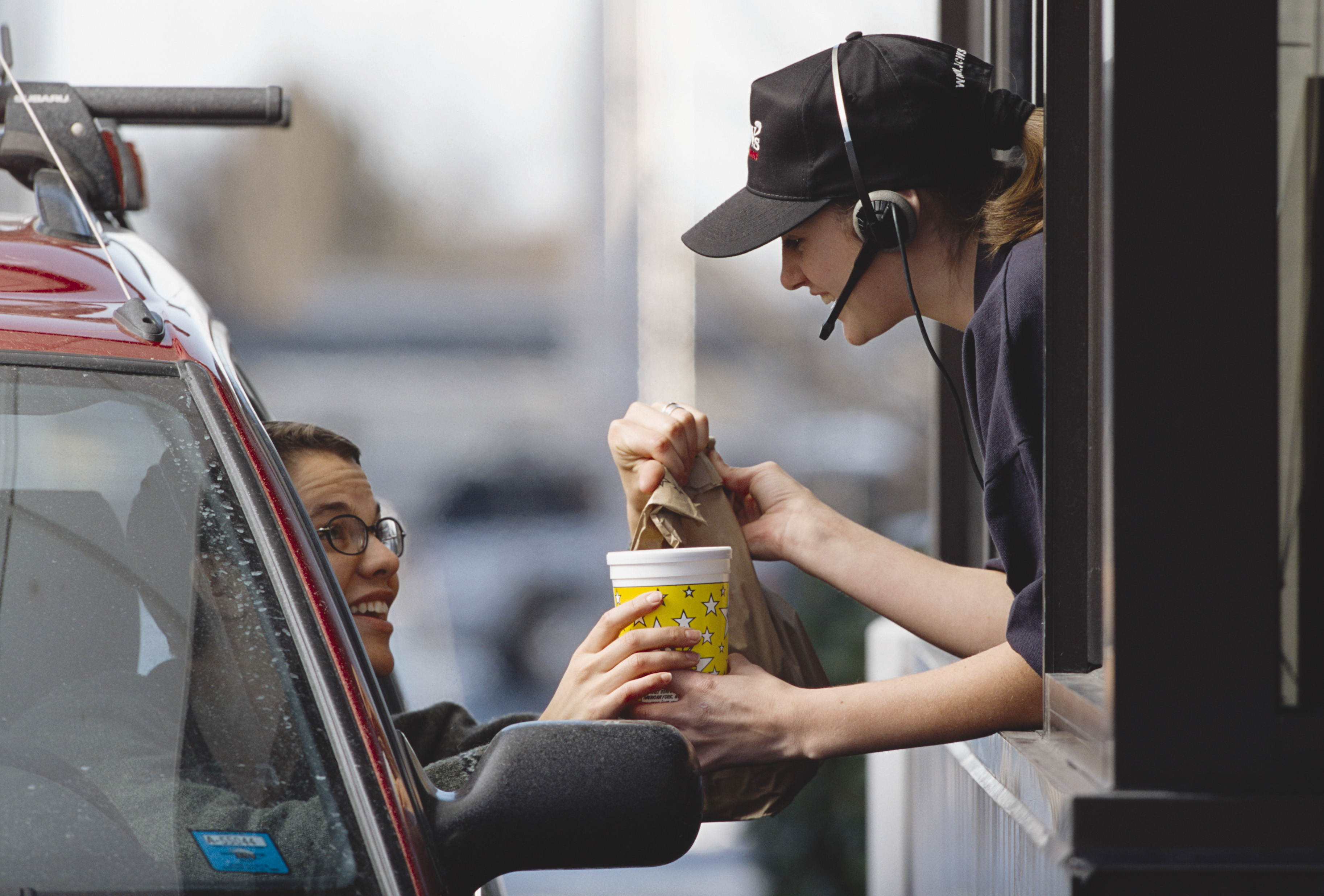 A woman handing a customer their food order at the drive-thru