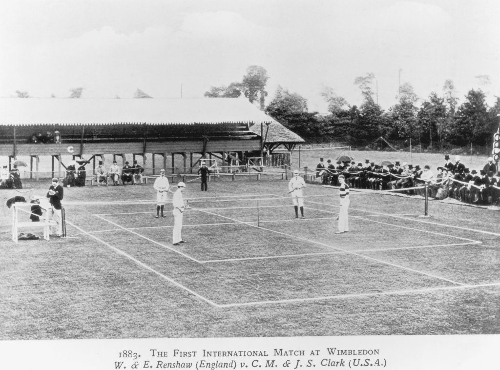 A sparsely attended match on a small court on grass; the men are in long pants