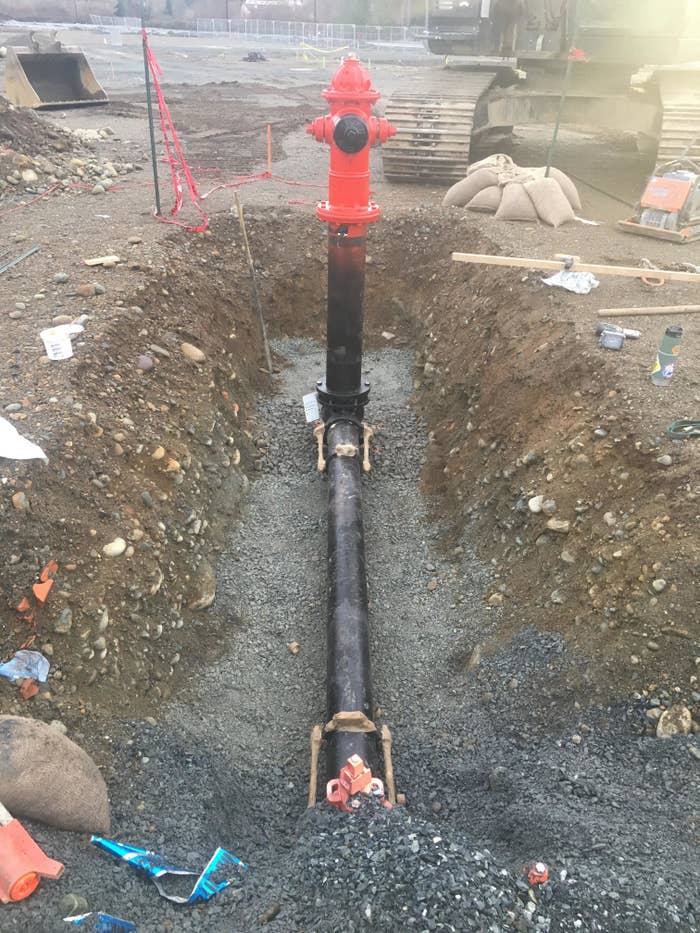 A huge hole in the ground showing a long pipe extending through the ground from the hydrant