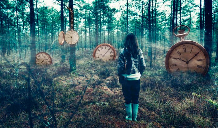 A woman standing in a forest surrounded by clocks