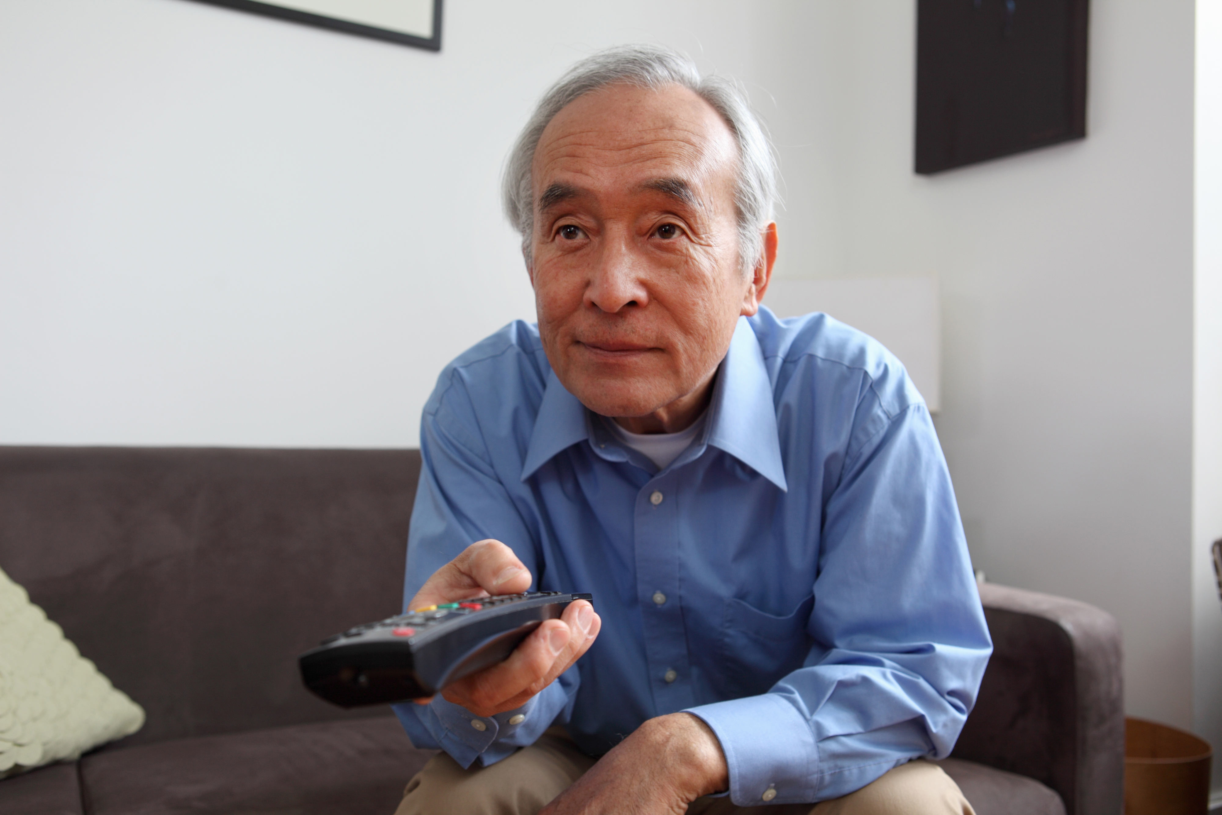 An older man with a television remote in his hand