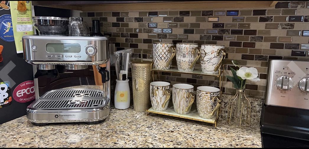 A stainless steel espresso machine on a granite counter top next to coffee mugs