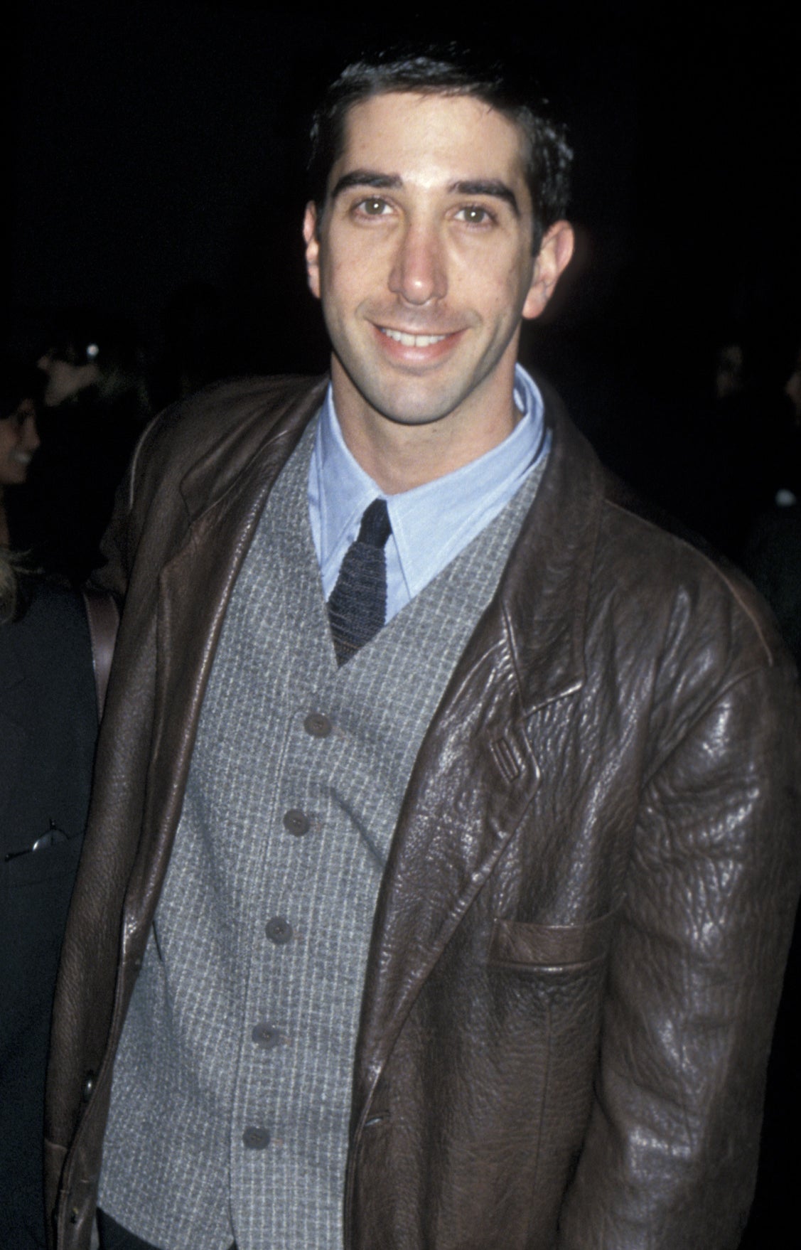 wearing a leather jacket over a button-down and vest