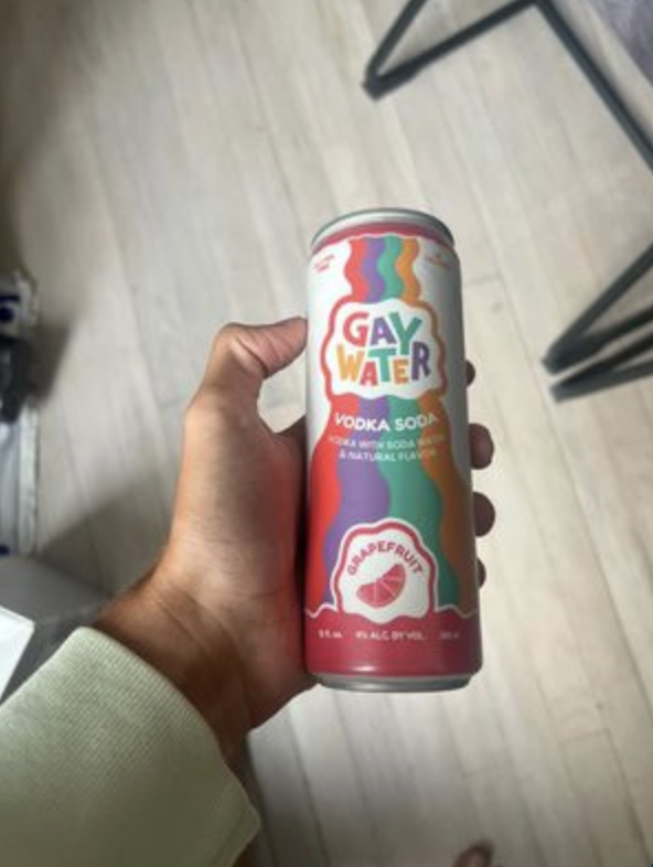 a man holding a can of vokda soda called Gay Water