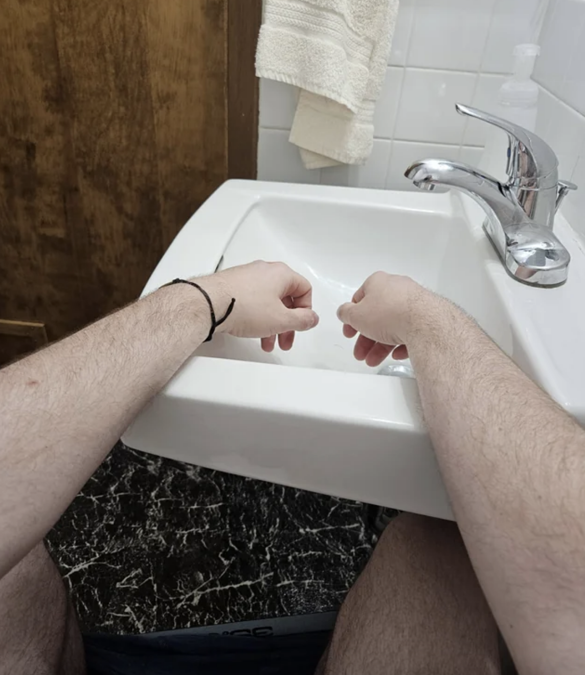A photo taken from the perspective of someone sitting on the toilet. They can easily place their hands in the sink from where they&#x27;re seated.
