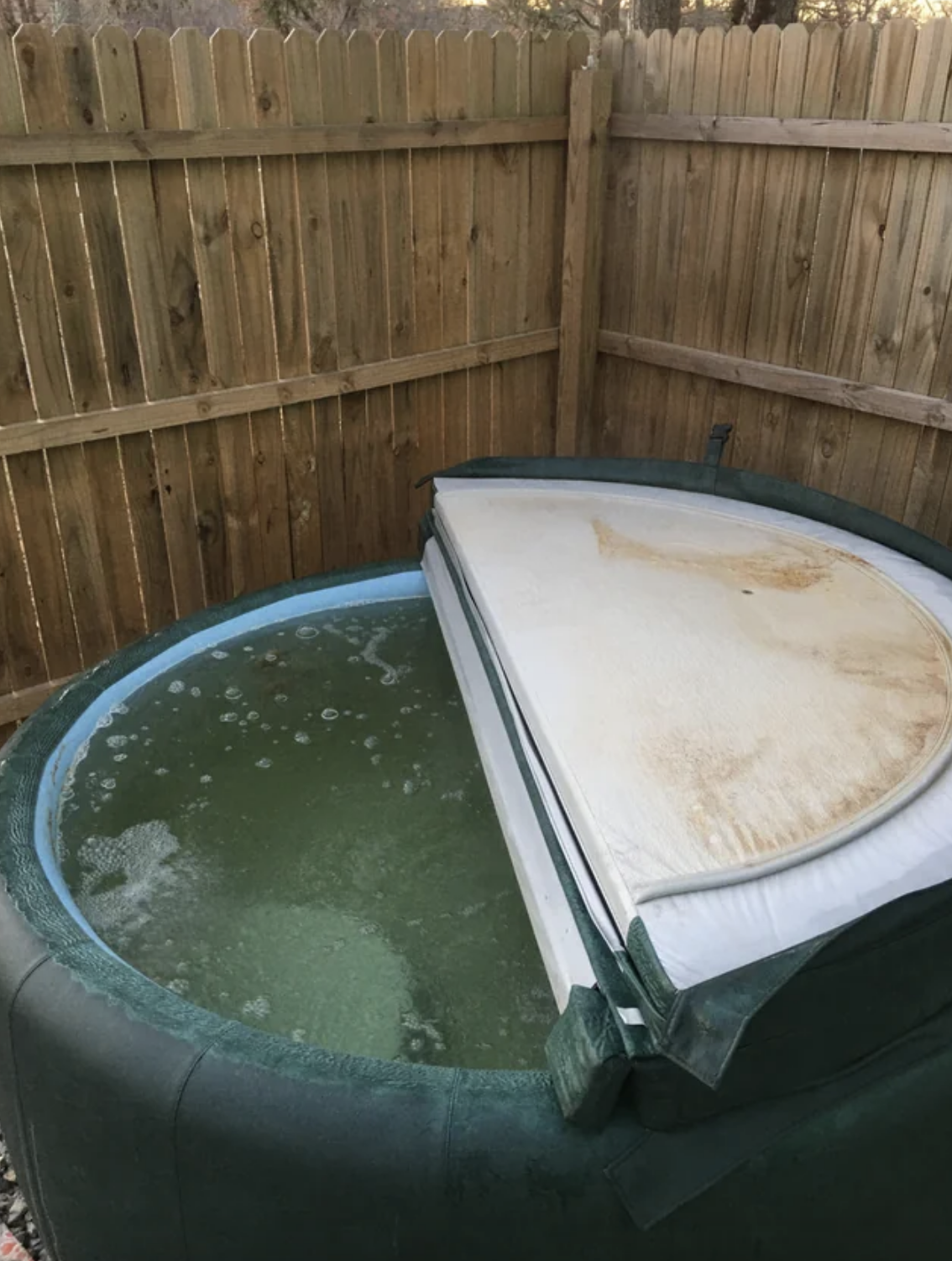 The cover of the hot tub is pulled back to reveal the bottom of the cover and the inside of the water are covered with dirt