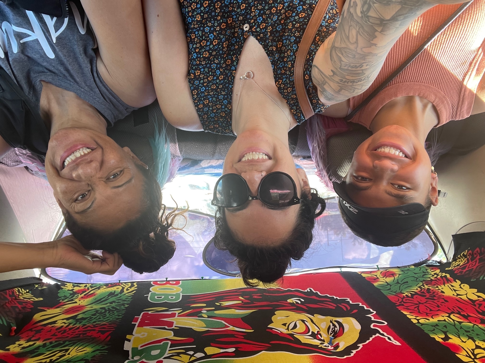 Three smiling women in the back of a car with a Bob Marley–themed interior roof