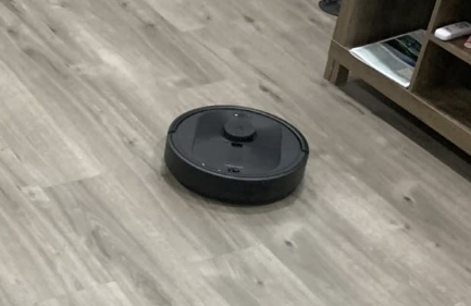 A circular black robotic vacuum on a vinyl gray floor