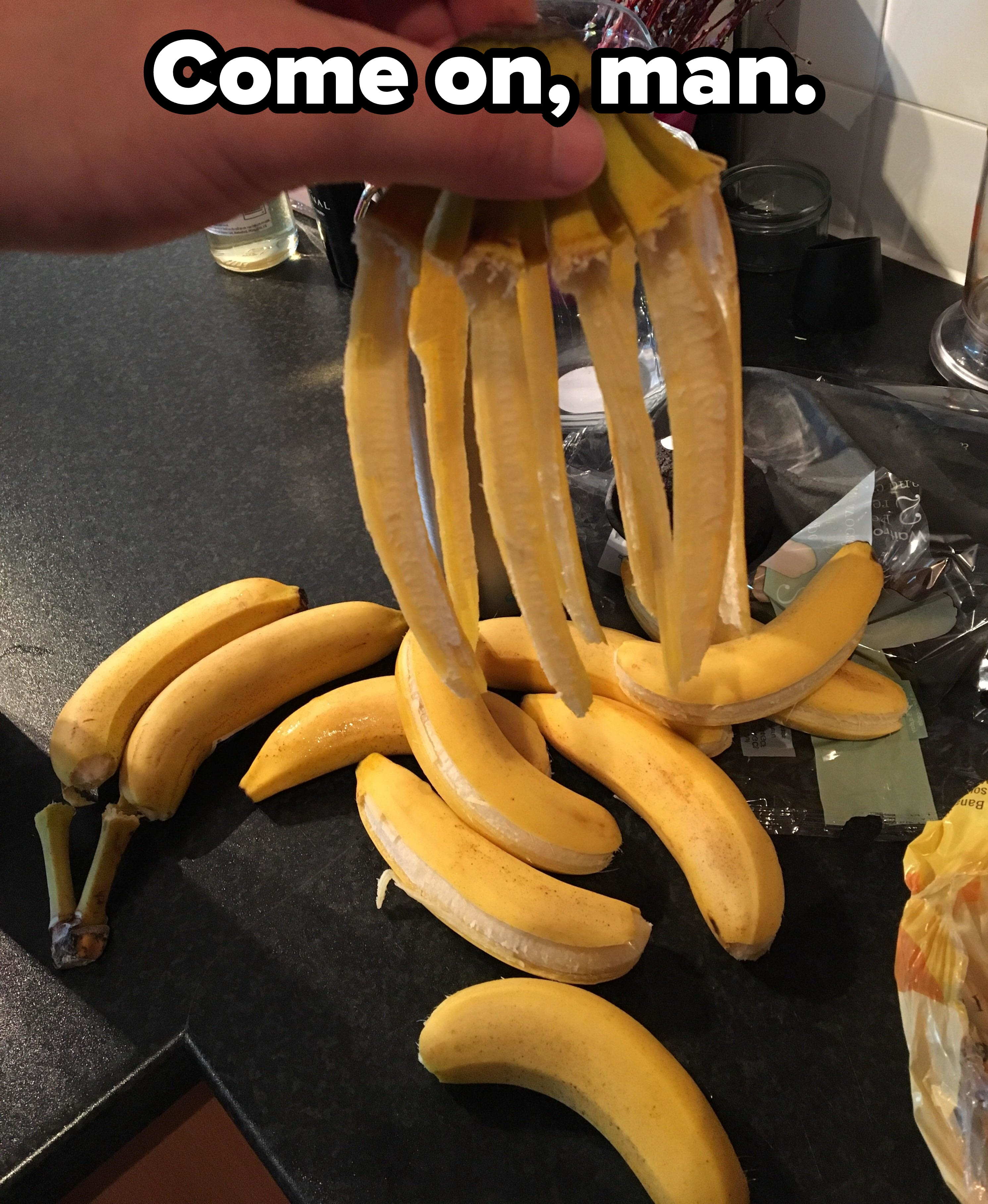 Each of the bananas in a hanging bunch is stripped of one part of its peel and falls to the counter surface