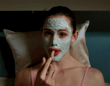 Jennifer Garner sitting up in bed, wearing face cream, and eating a cheese puff