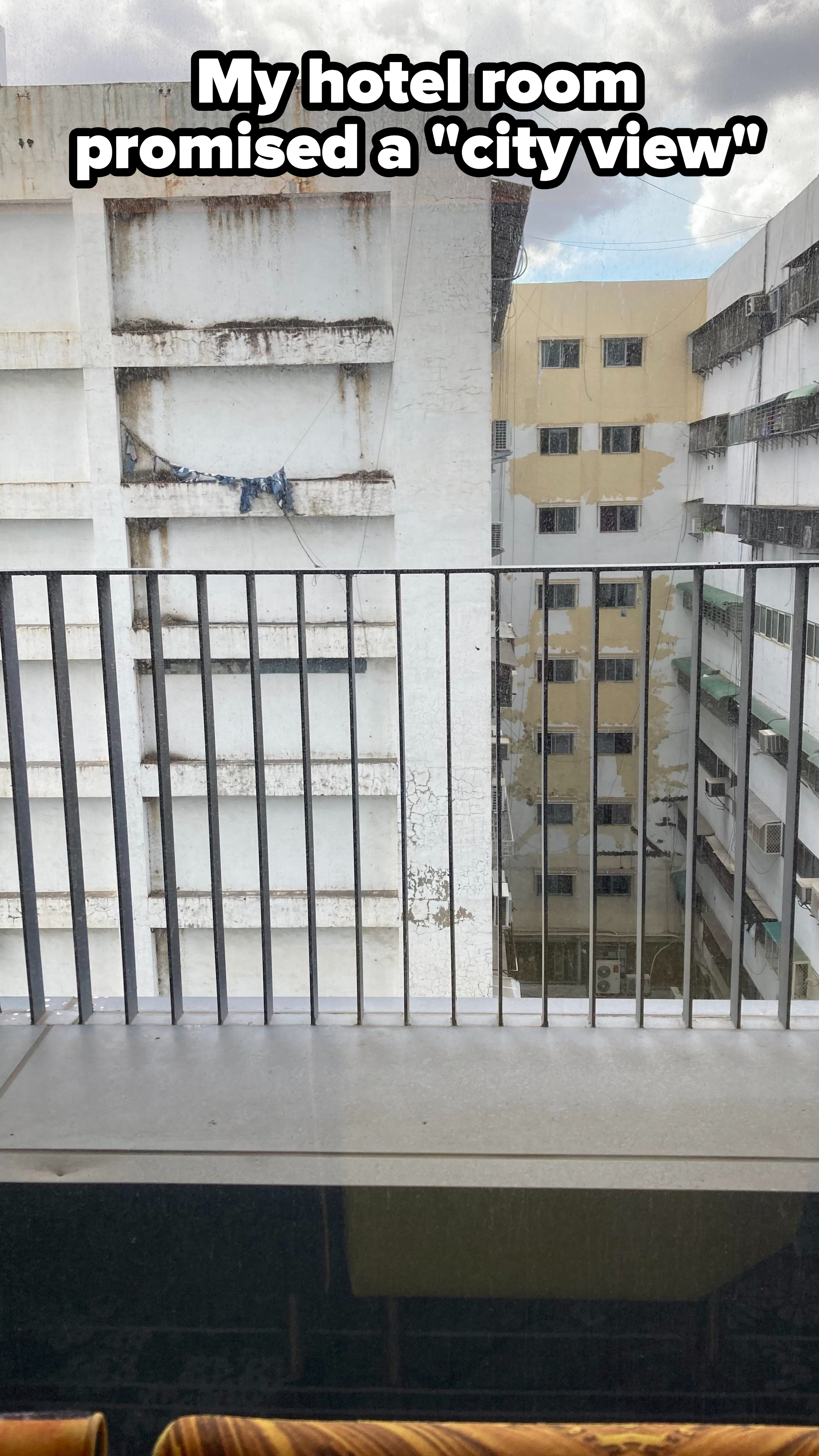 The back of a gray, nondescript, badly painted, boarded-up building seen from a balcony, with the caption &quot;My hotel room promised a &#x27;city view&#x27;&quot;