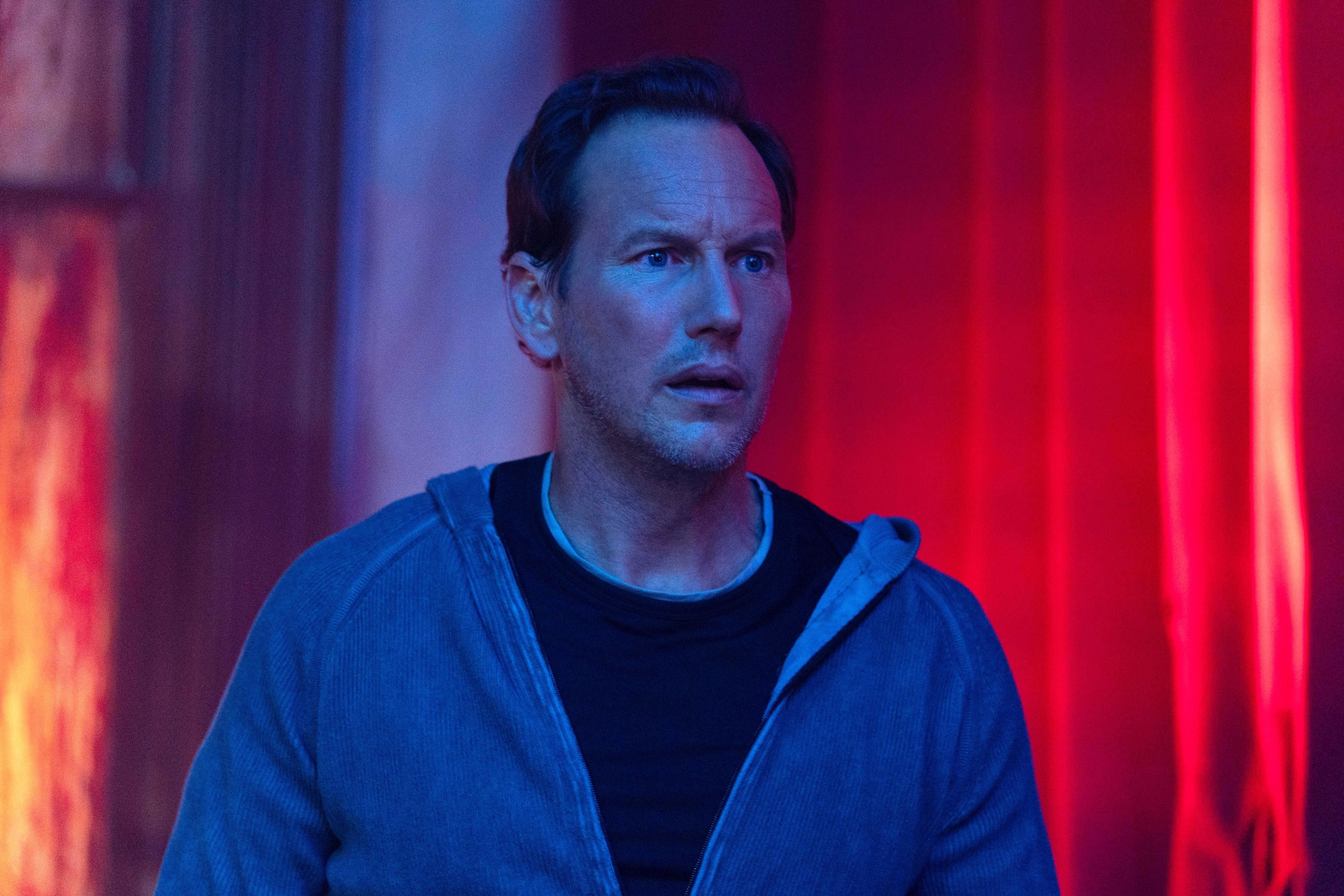 Patrick Wilson stands in a strange red room while soaked in blue light