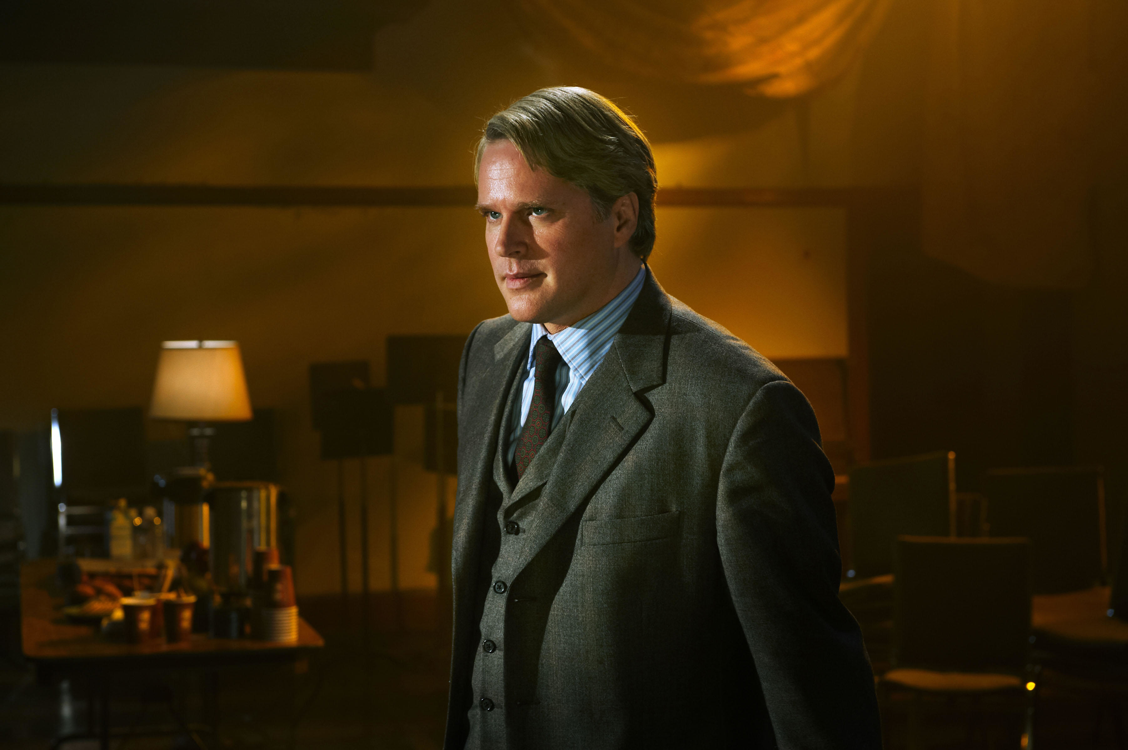 A well-dressed Cary Elwes stands ominously in a dark office