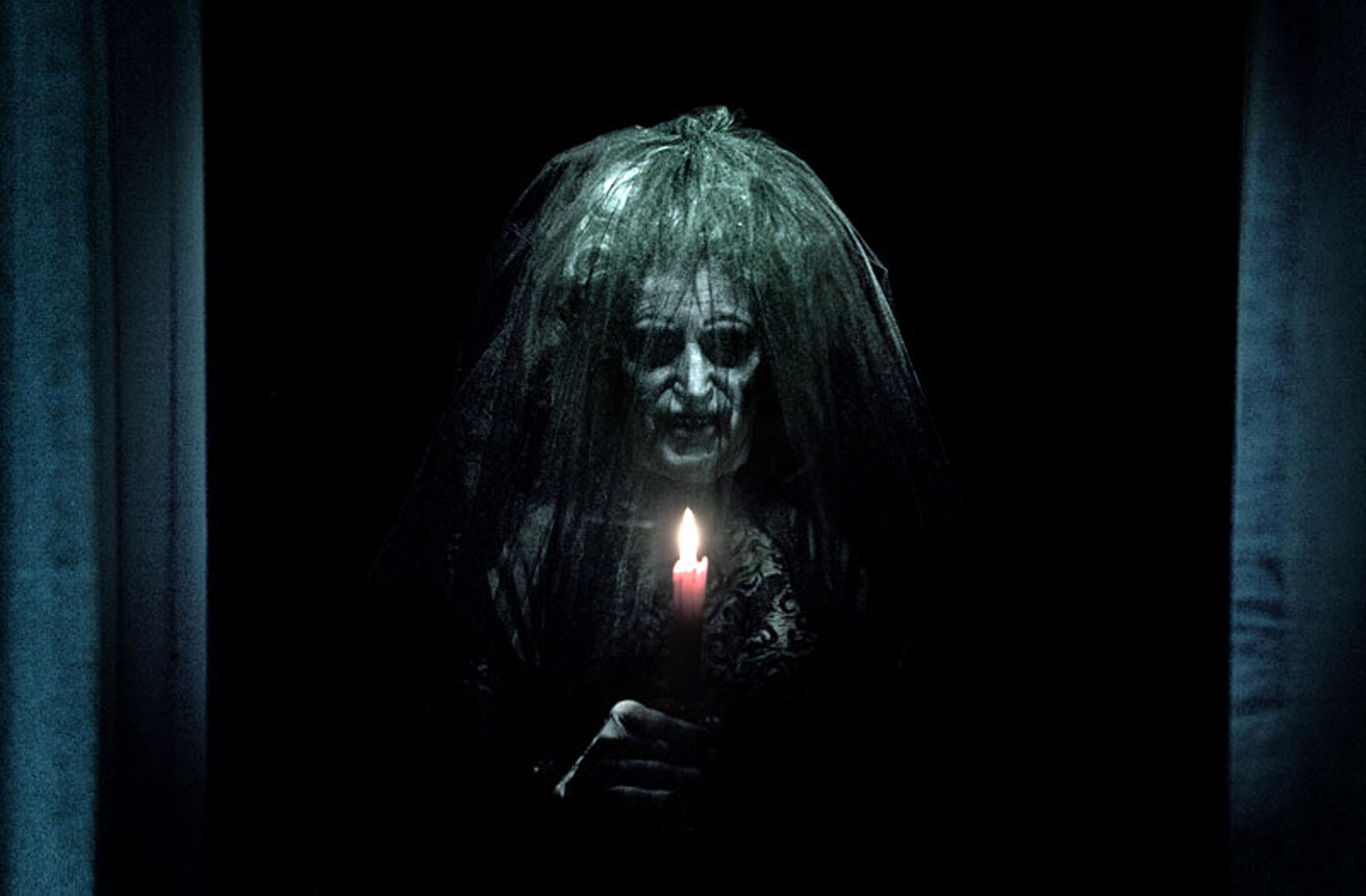 An old woman in a black dress holds a candle to her face
