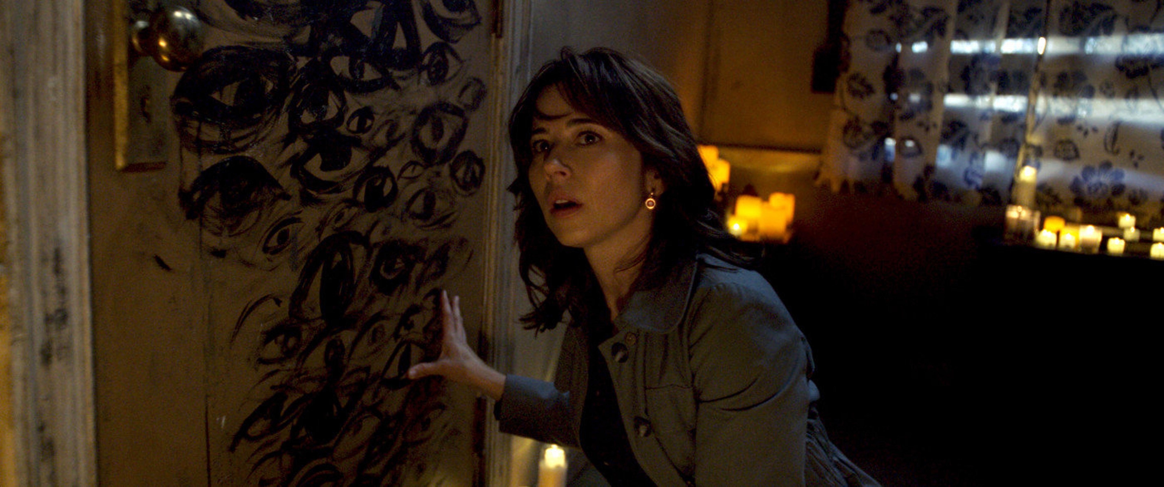 Linda Cardellini looks around a dirty room covered in candles and creepy markings