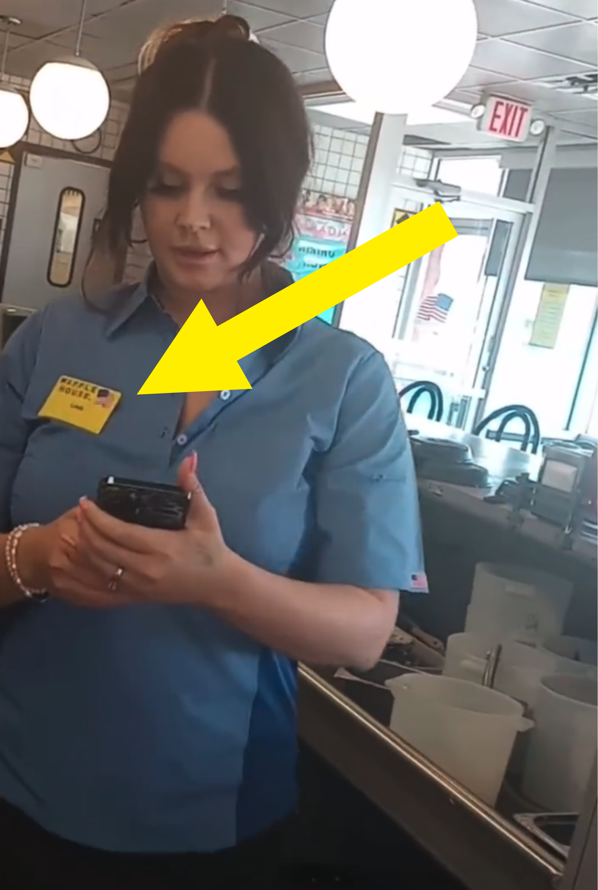 arrow pointing to the nametag on her shirt as she looks at her phone