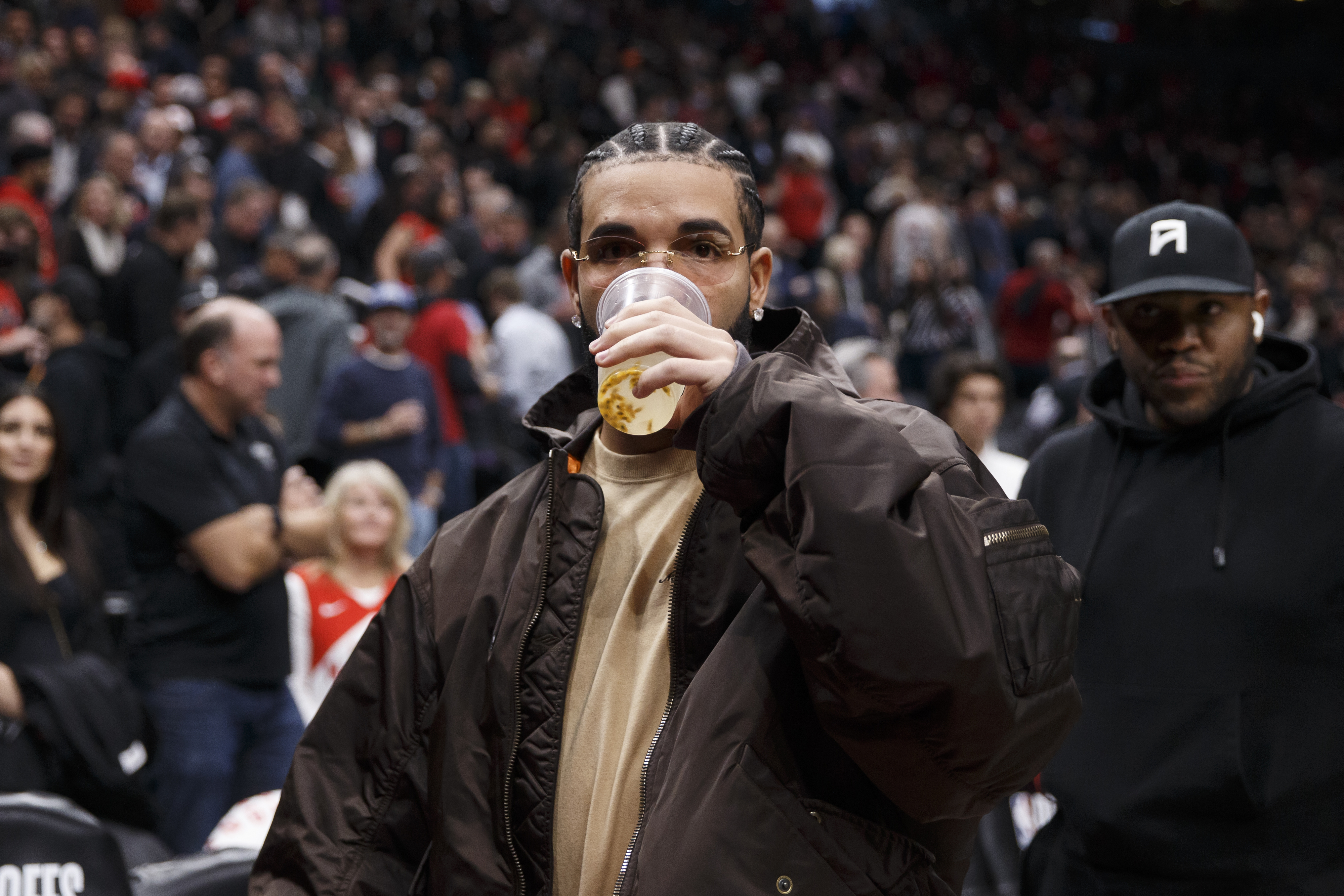 drake taking a drink from his cup at a basketball game