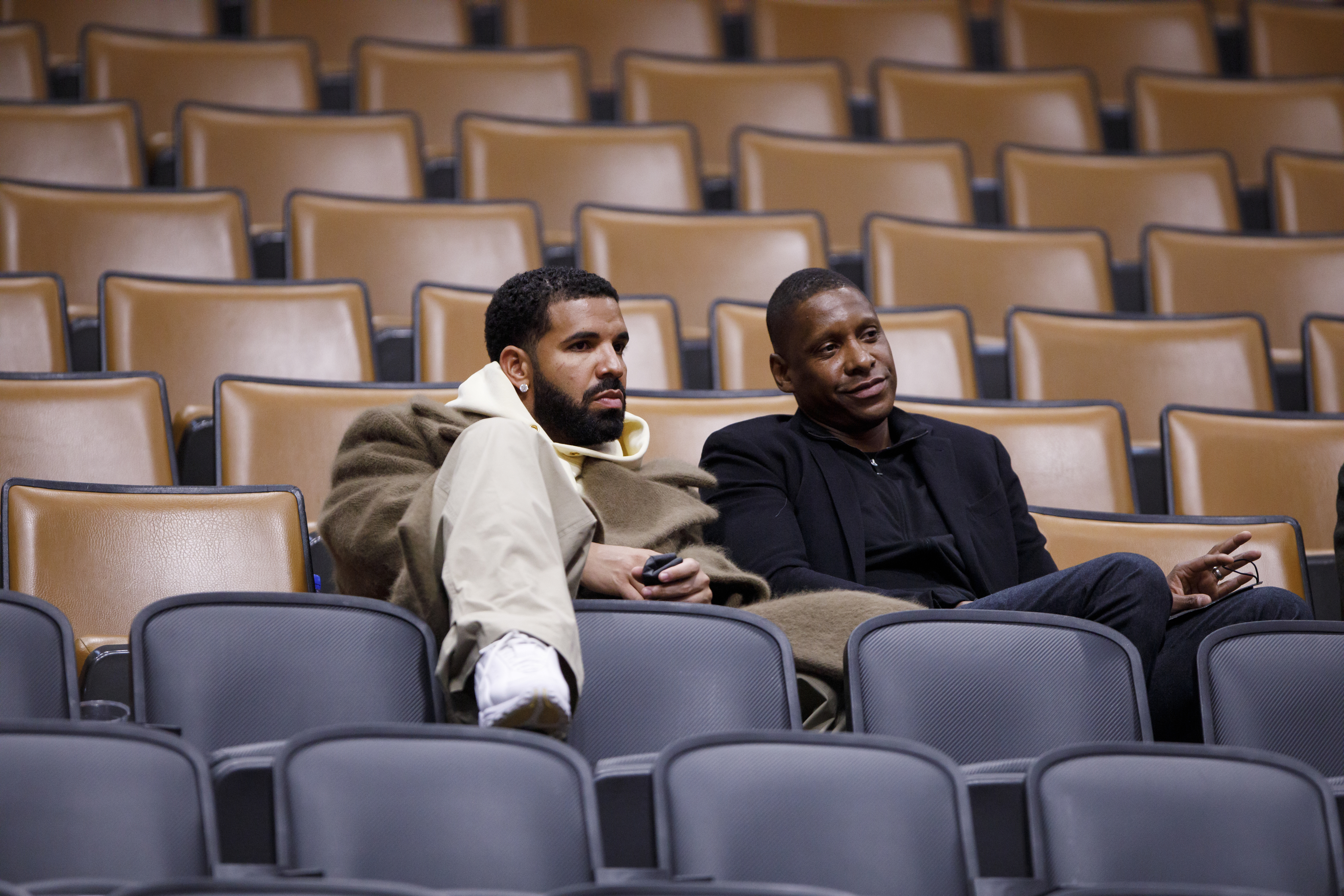 drake sitting in otherwise empty stadium seats with another man