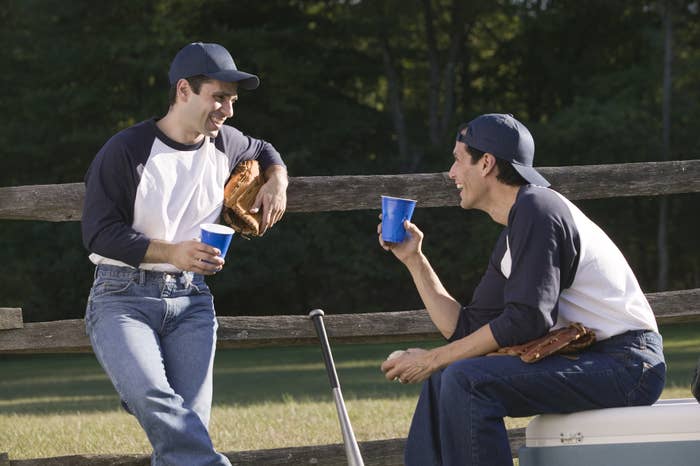 Two baseball players drinking from blue cups and talking and laughing