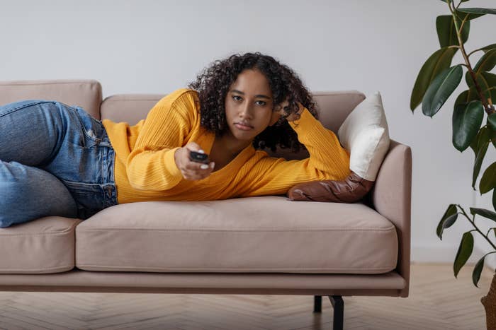 A woman with a remote in her hand laying on the couch