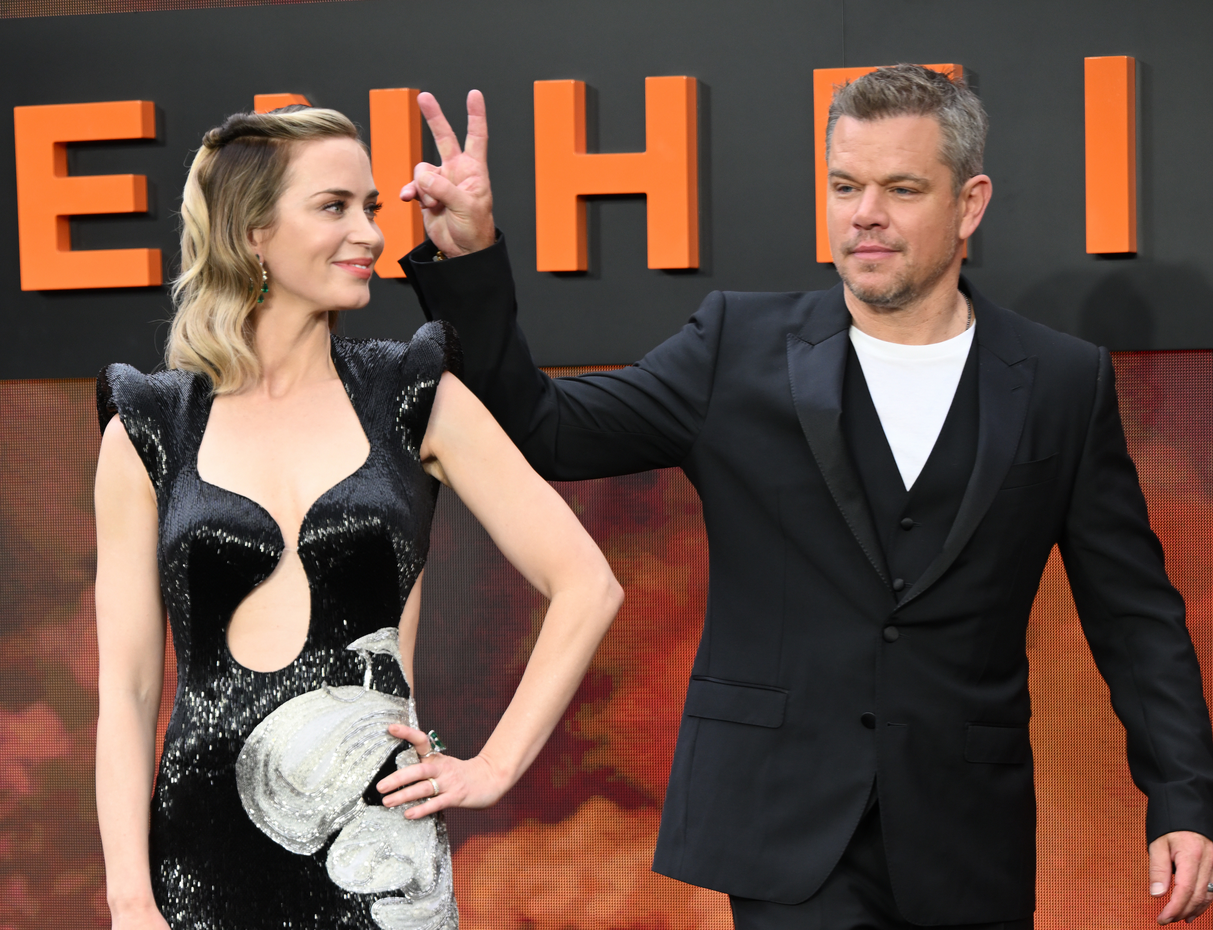 Emily poses while Matt throws up a peace sign at a press event for the movie