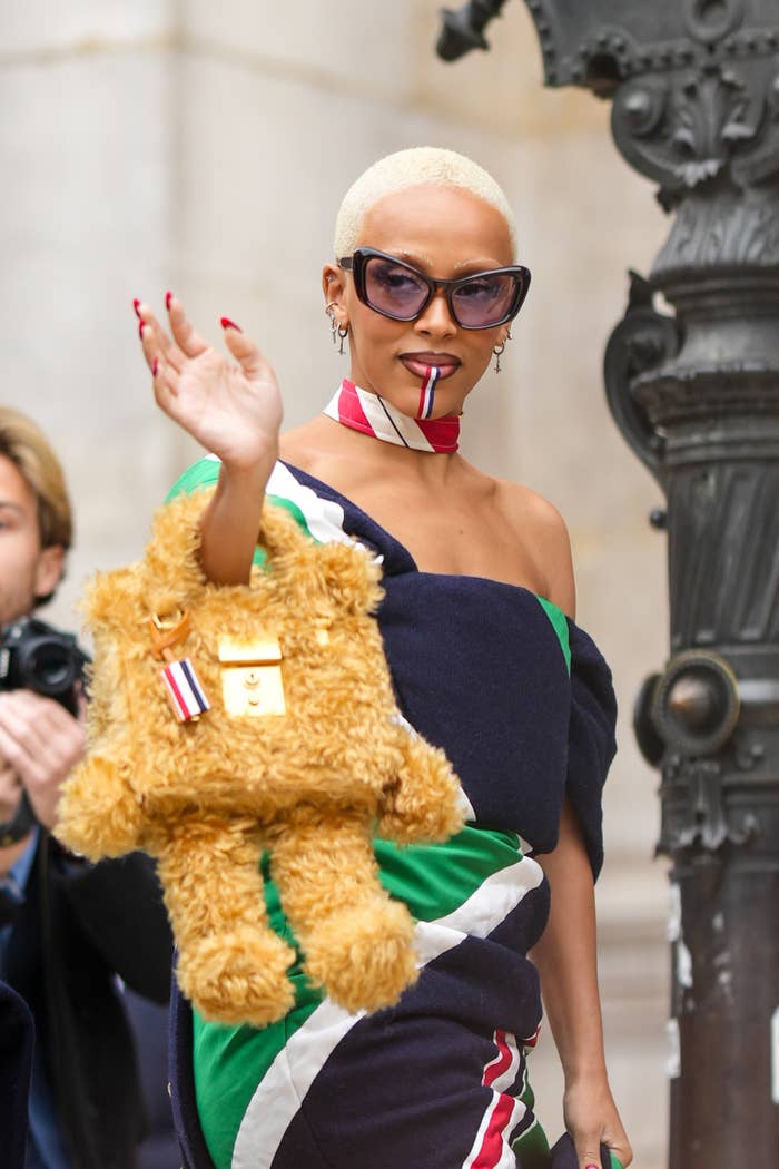 Doja Cat waving to the crowd while holding a teddy bear shaped purse