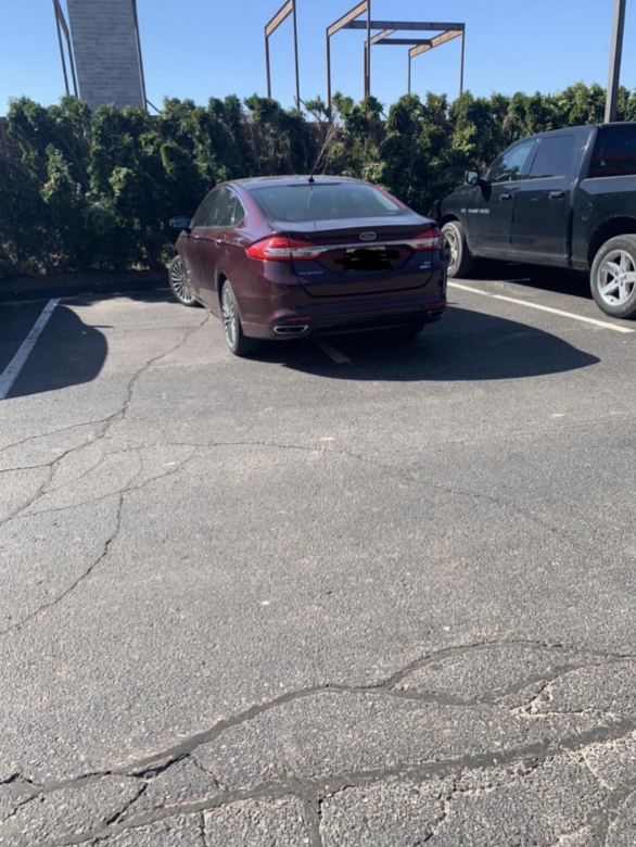 A car in the parking lot is parked with the line of the spot right in the middle of the car, taking up as much of two adjoining space as possible