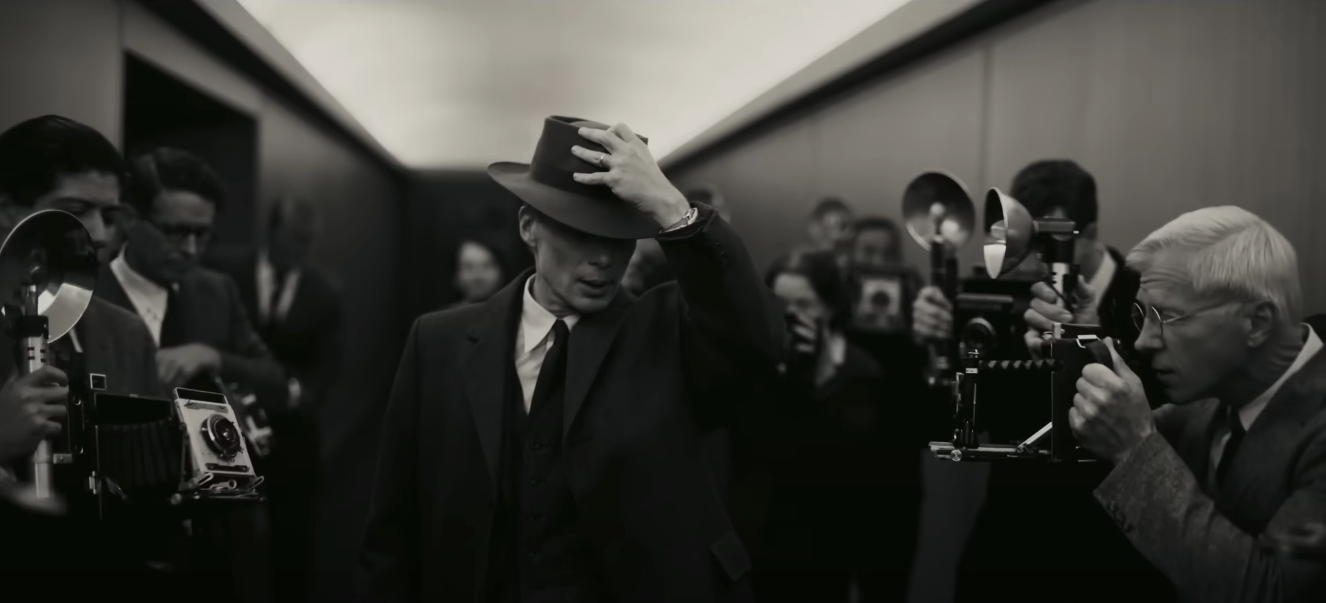 Oppenheimer walks down a hallway as he&#x27;s surrounded by photographers