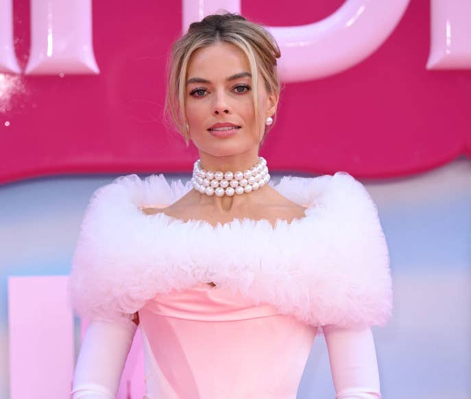 Closeup of Margot Robbie in a long-sleeve corset gown with a tulle trim and a three-string pearl necklace