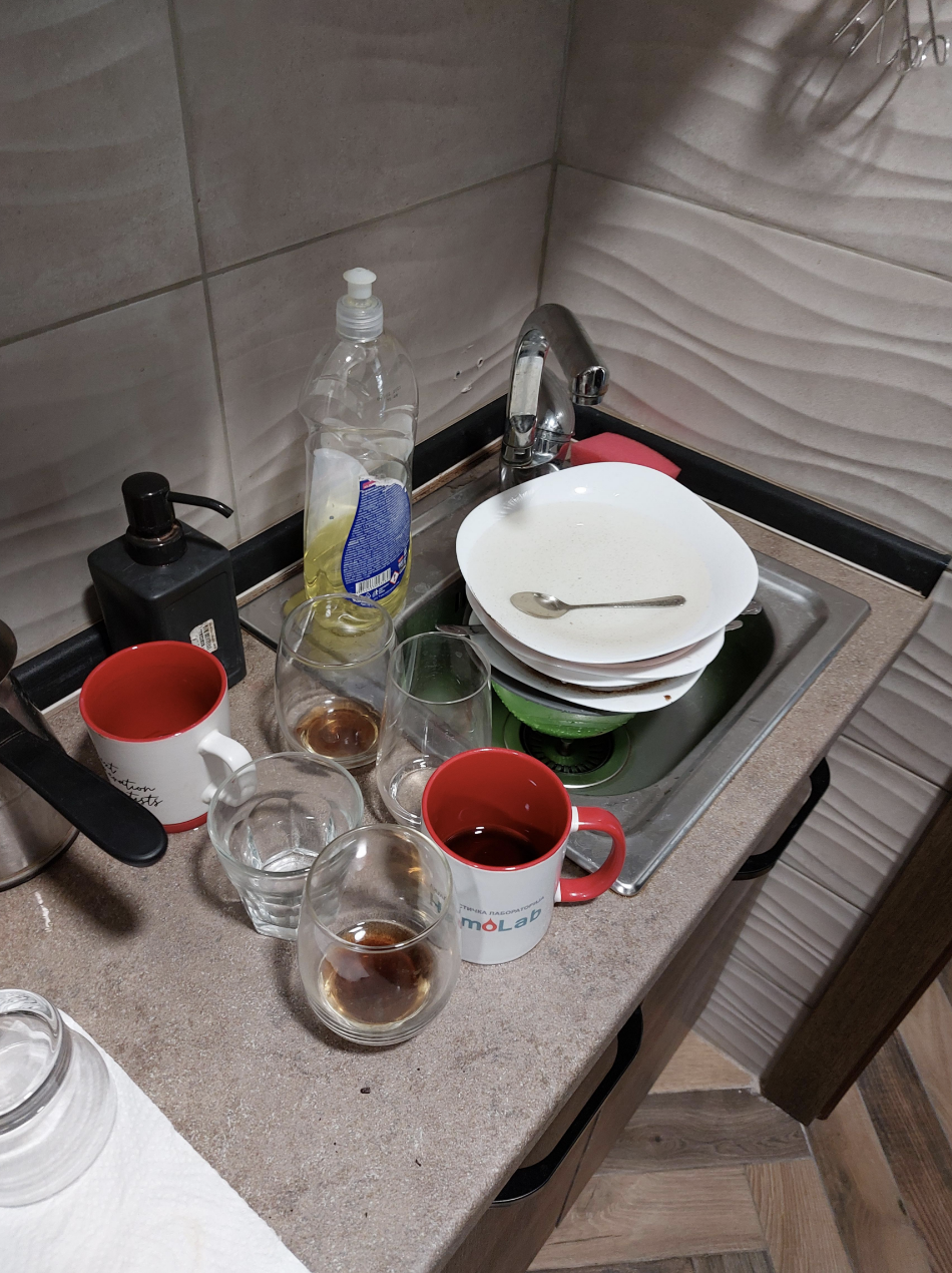 The sink is full of plates and silverware, so used mugs and glasses are being lined up on the counter