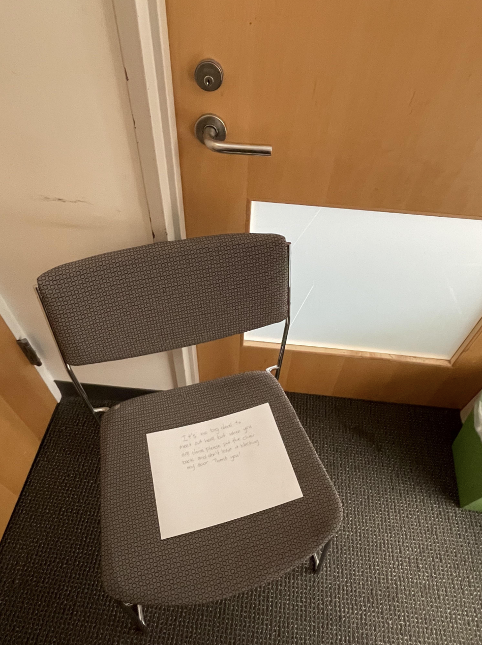 A chair sitting so close to a door that it&#x27;s not possible to open the door; the chair has a note on it