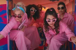 Margot Robbie and Alexandra Shipp as Barbies, Michael Cera as Allan, America Ferrera as Gloria, and Ariana Greenblatt as Sasha all wearing jumpsuits and sunglasses in the back of a car