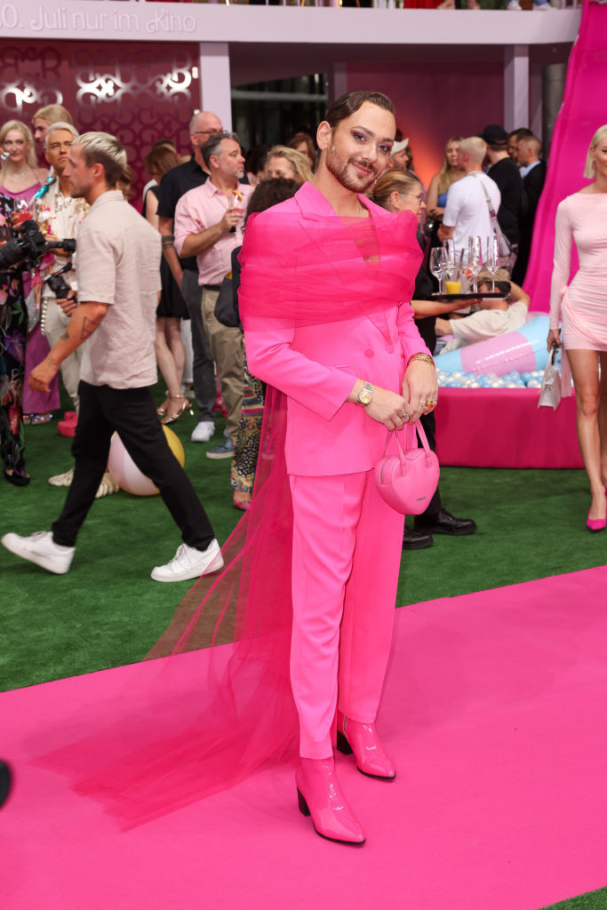 in a pink suit with pink boots and a tulle wrap around his shoulders going down to the floor