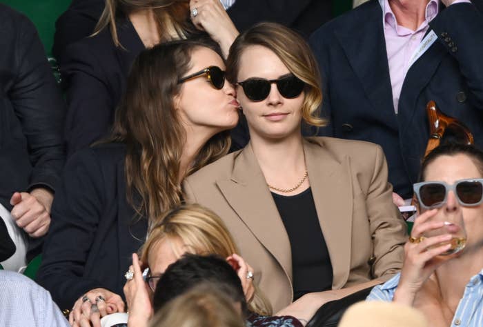 Closeup of Minke playfully kissing Cara Delevingne on the cheek as they watch an event