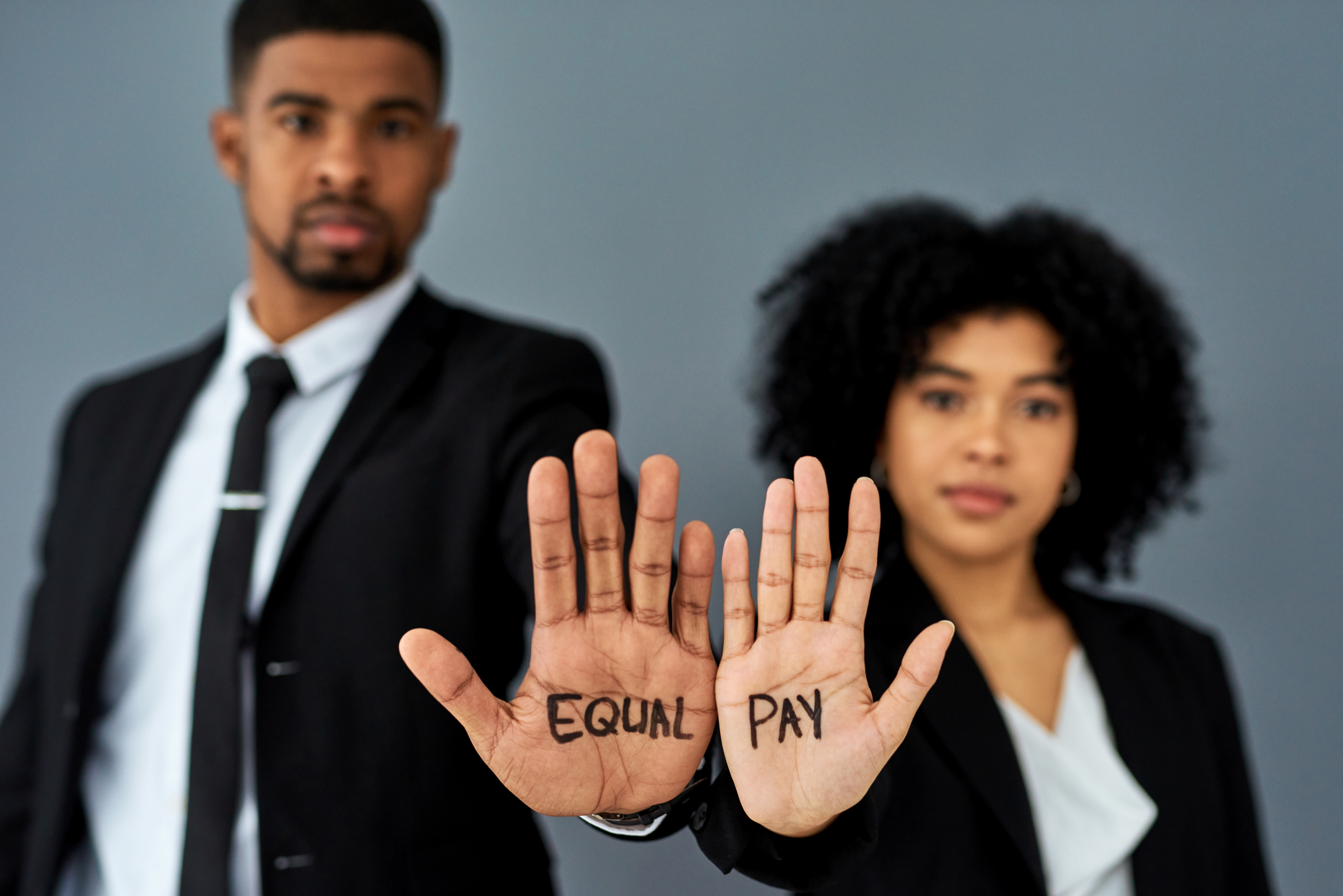man and woman in business attire with equal pay written on their hands