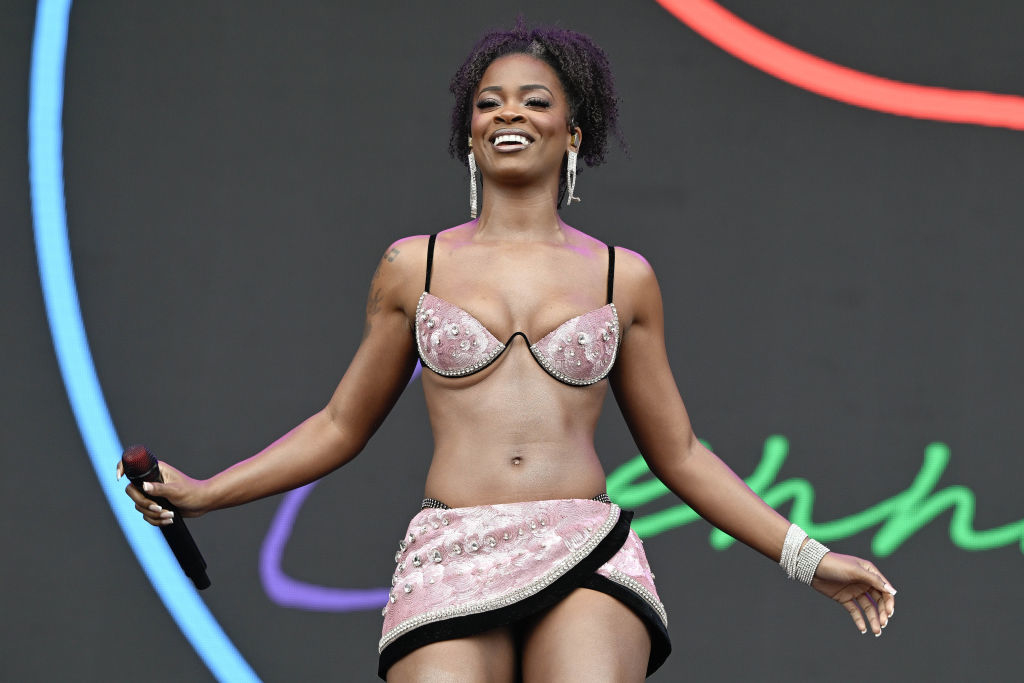 Ari Lennox onstage performing in a bra-style top and a mini wrap skirt
