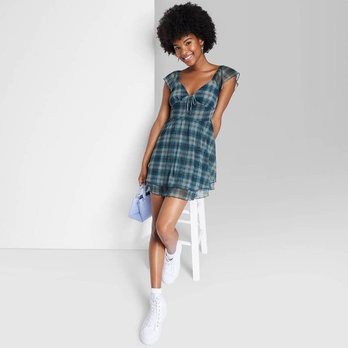 model in a blue and black plaid dress with sheer flutter sleeves and overlay