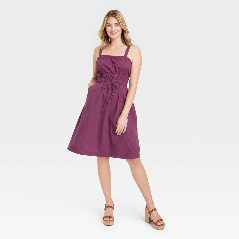 model in plum knee length fit and flare dress with waist tie