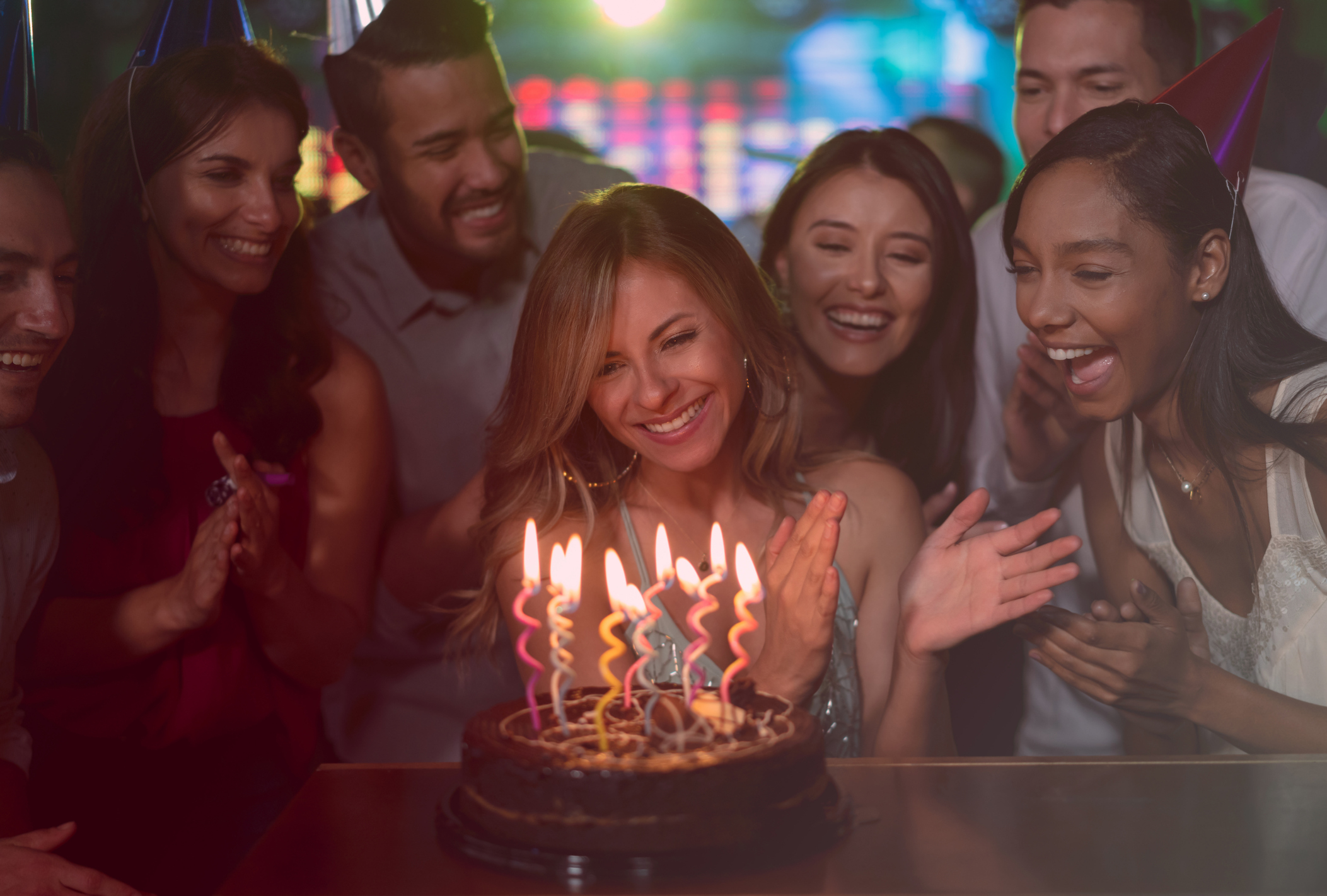 People singing happy birthday to a woman with a cake with candles in front of her