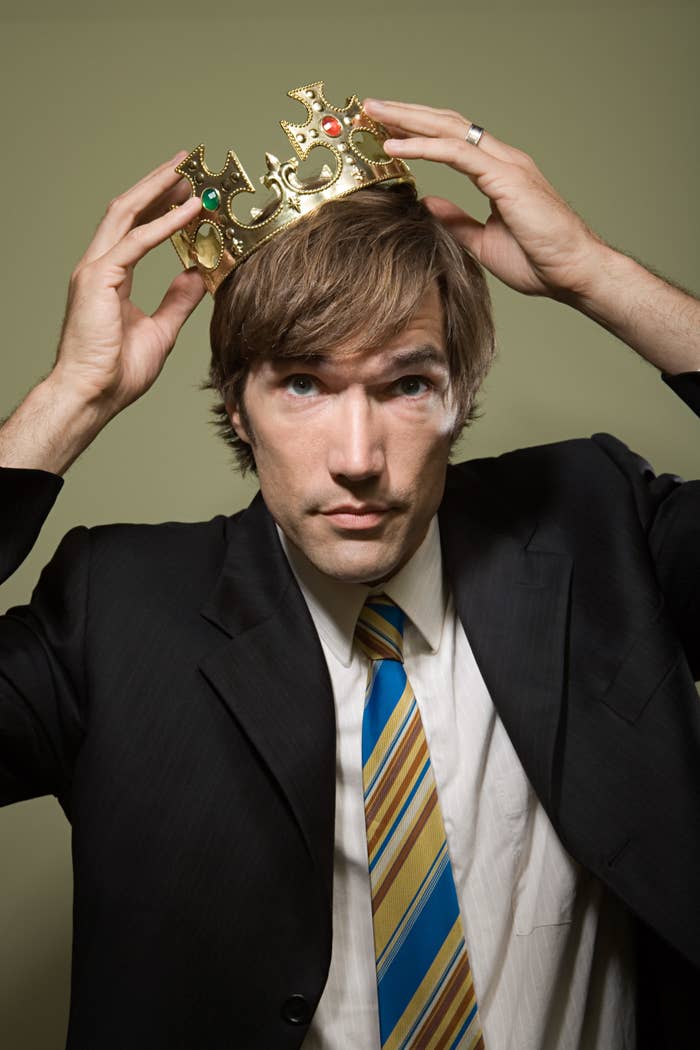 Man in a suit holding a crown on his head
