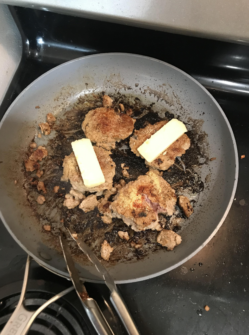 A look inside a pan in which four burger patties have been overcooked and the dry spices used have also been overcooked and covered the pan in a layer of soot