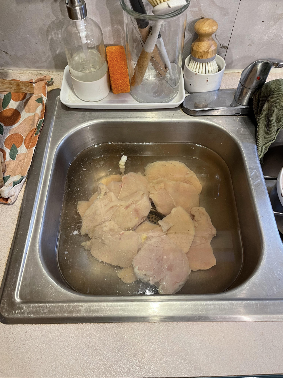 Several raw chicken thighs sit submerged in water in a sink