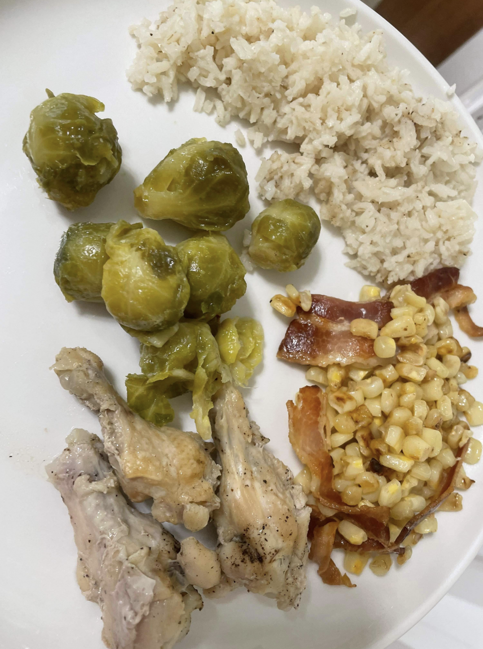 This plate has corn, Brussels sprouts, rice and chicken drumsticks, and they all look undercooked
