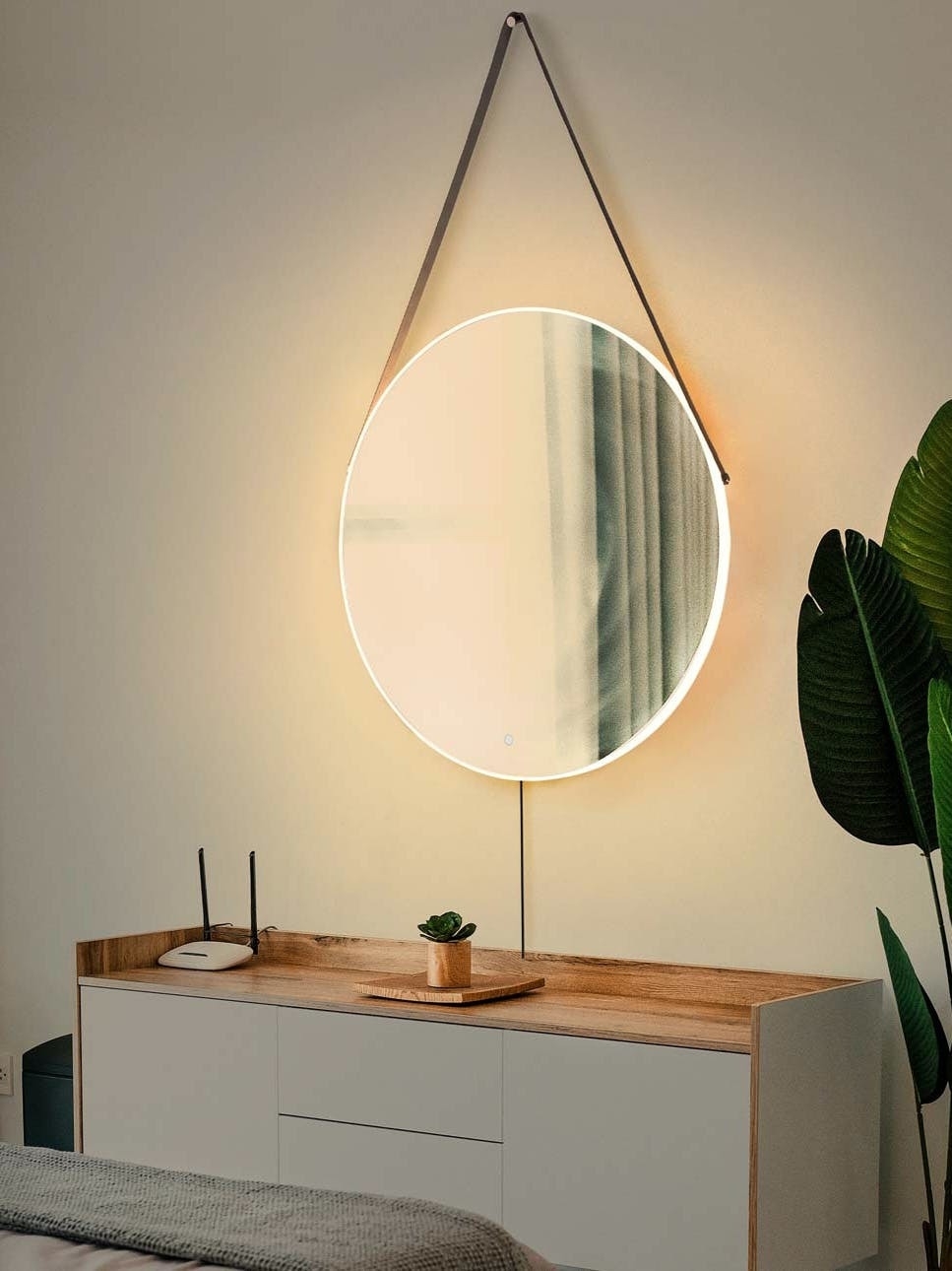 A hanging round mirror with a light over a dresser.